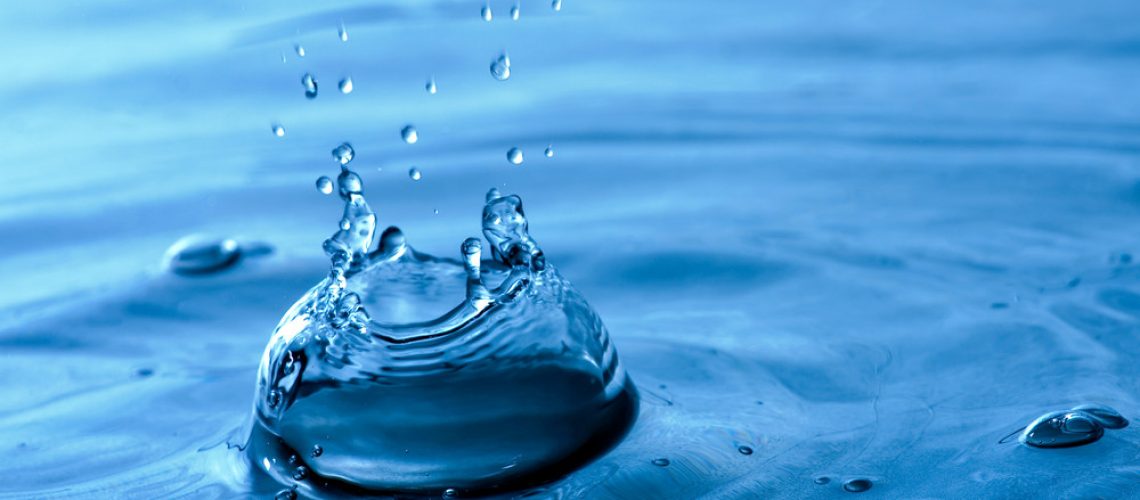 A blue water background texture and splash with droplets forming a crown shape. Shallow depth of field.